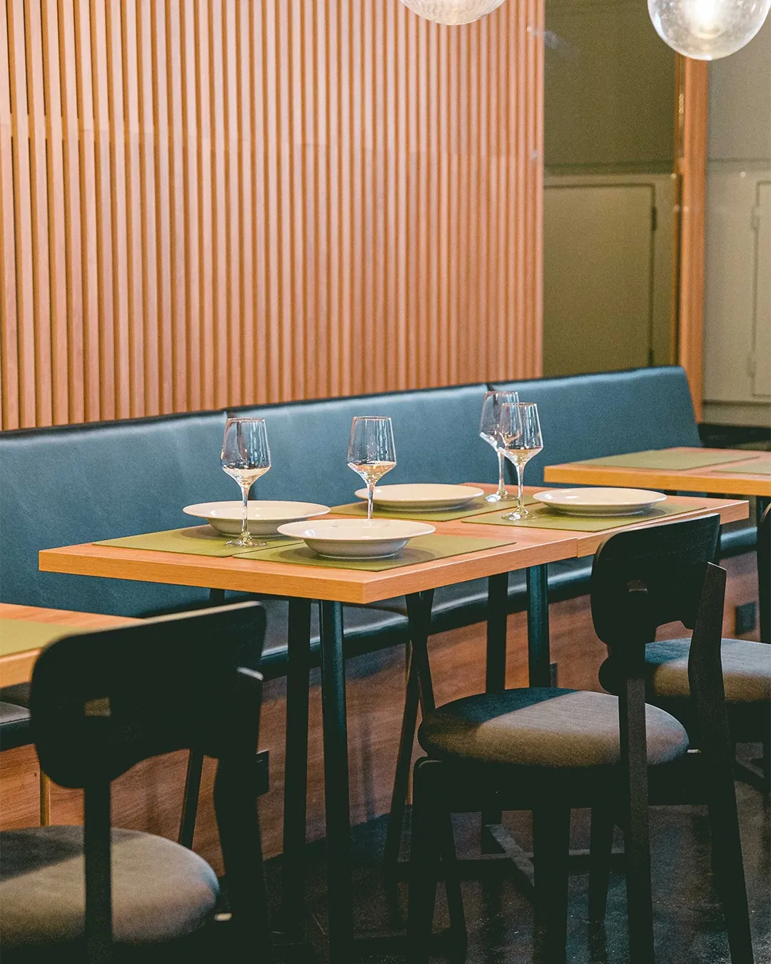 Una mesa preparada con platos y copas, junto al banco del salón de Oliva
