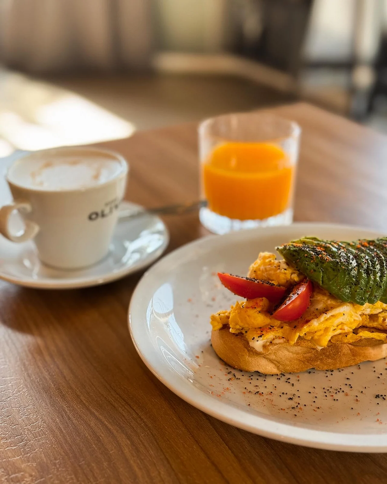 Café, jugo y tostón de pan de campo con queso crema, huevo, cherry y palta en Oliva